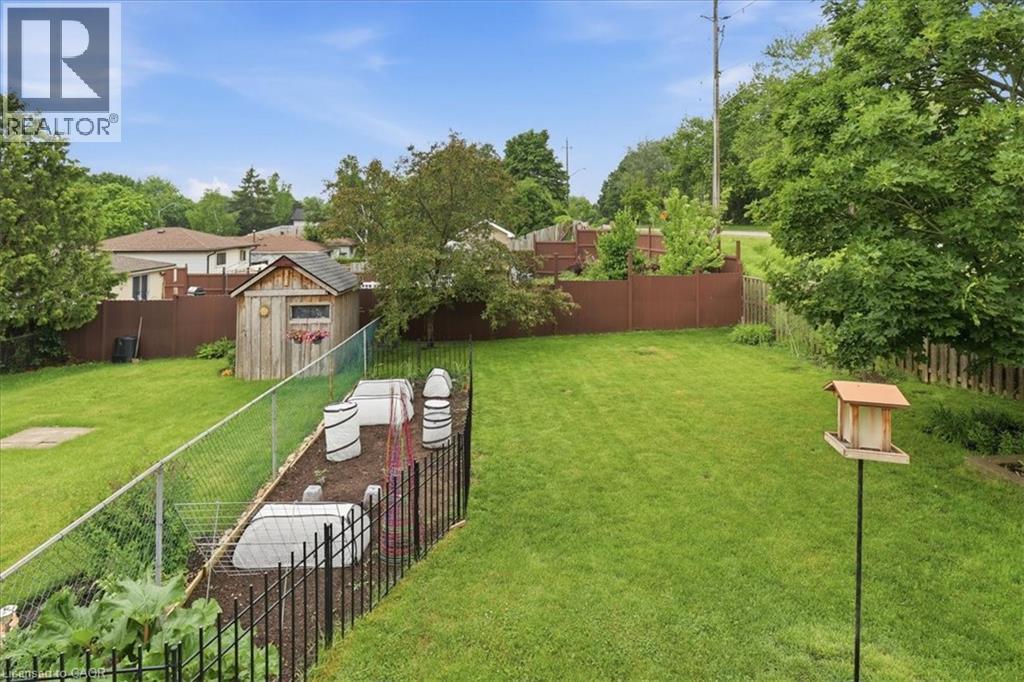 Expansive backyard featuring a manicured lawn, dedicated garden beds, a chain-link fence, and a wood storage shed - 116 Scott Road, Cambridge, ON