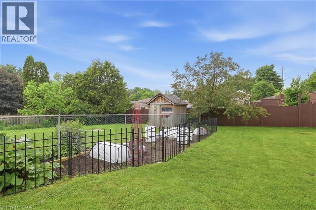 Expansive green lawn with a dedicated garden area, featuring a decorative black metal fence - 116 Scott Road, Cambridge, ON