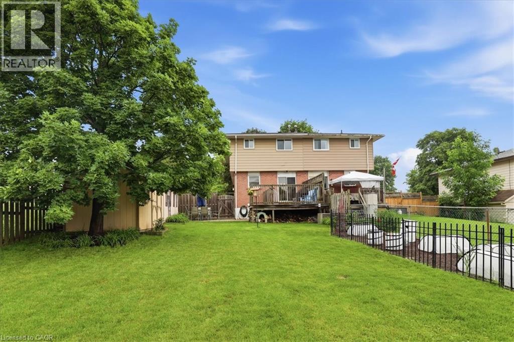 Expansive backyard featuring a large green lawn, mature trees, and a multi-level wooden deck - 116 Scott Road, Cambridge, ON