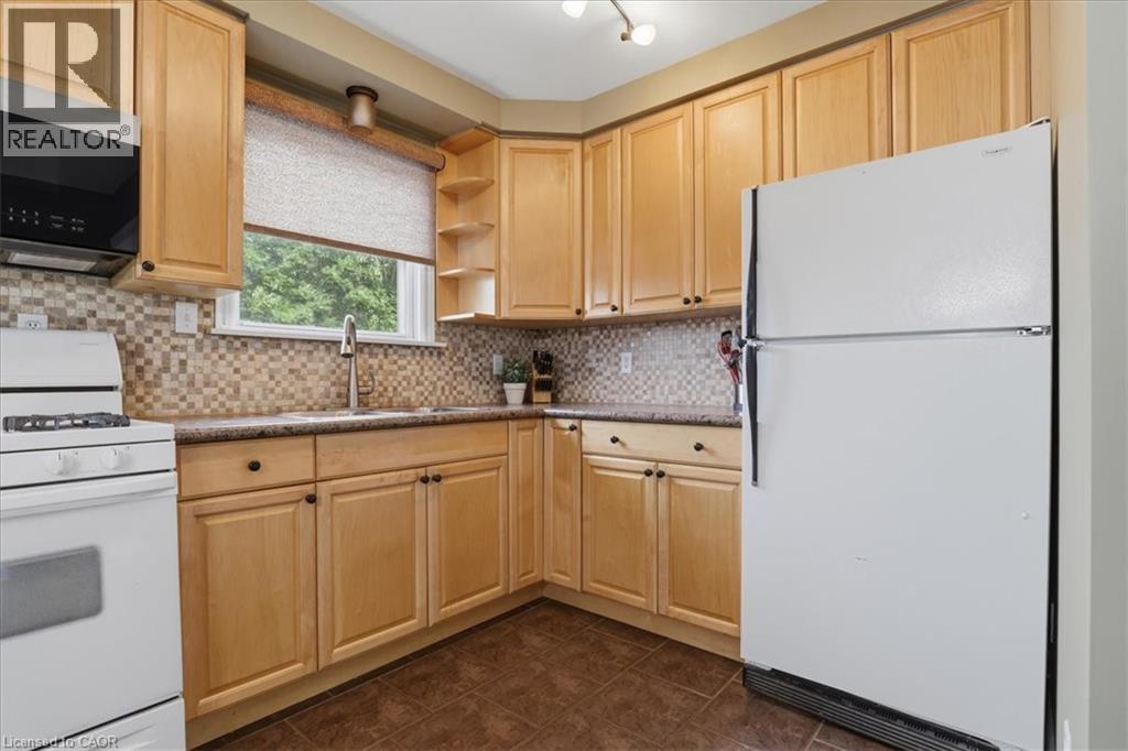 Kitchen featuring light wood cabinetry, mosaic tile backsplash, solid surface countertops, and a window above the sink - 116 Scott Road, Cambridge, ON