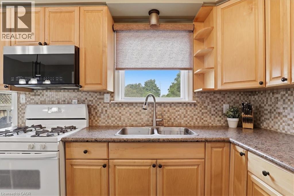 Kitchen featuring light wood cabinetry, stone-finish countertops, stainless steel sink with a gooseneck faucet, mosaic tile backsplash, and an over-the-range microwave - 116 Scott Road, Cambridge, ON