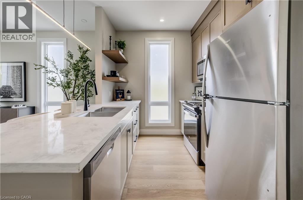 Modern kitchen featuring light wood-finish flooring, light cabinetry, and an island with a light-toned countertop and an undermount sink with a black faucet - 210 Heritage Drive Unit# Upper, Kitchener, ON