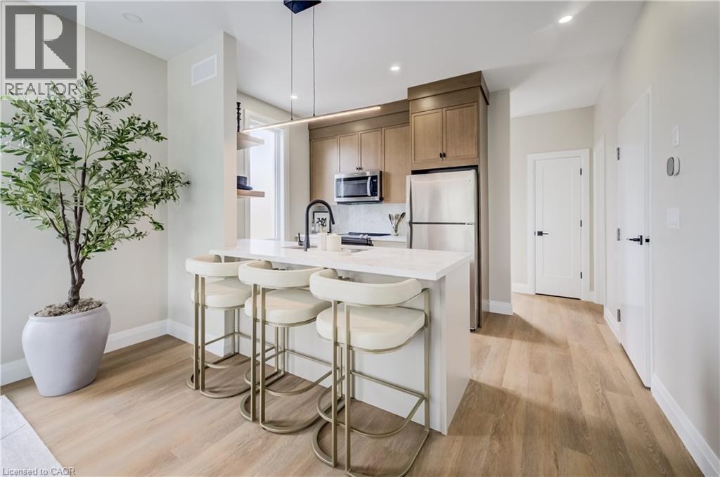 Modern kitchen featuring light wood-finish flooring, a white countertop island with seating, stainless steel appliances, and wood cabinetry - 210 Heritage Drive Unit# Upper, Kitchener, ON