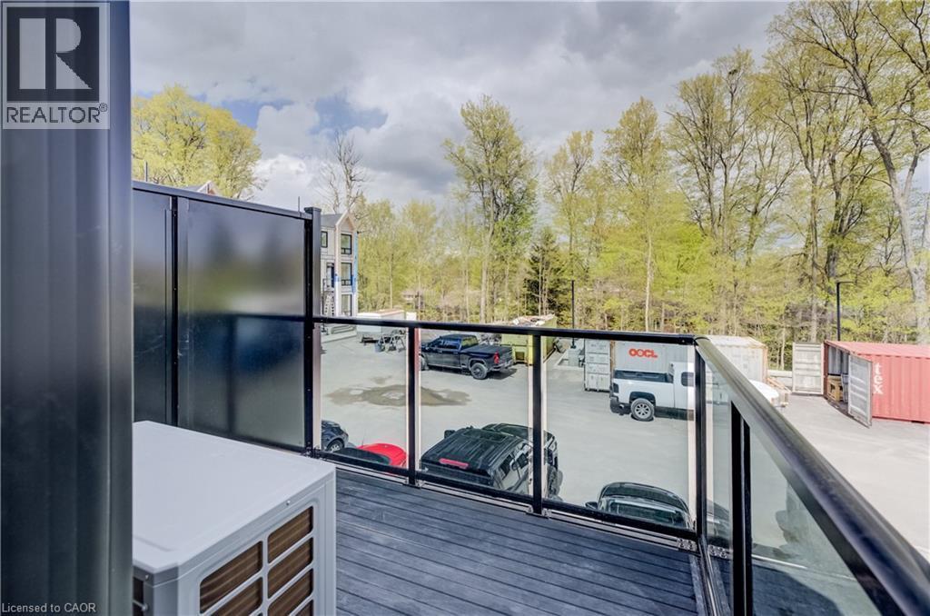 Private balcony with composite decking, modern glass railing, and black privacy paneling, offering treetop views - 210 Heritage Drive Unit# Upper, Kitchener, ON