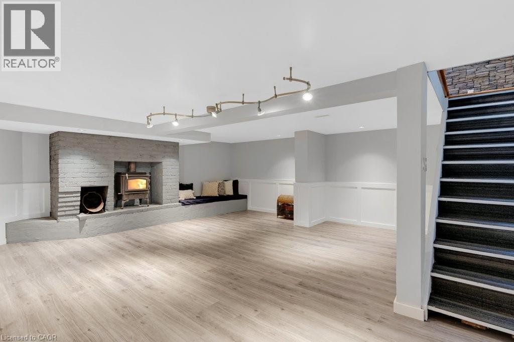 Expansive finished lower level featuring light wood-finish flooring, a painted brick fireplace with a wood-burning stove, and a built-in bench seating area - 3786 Old Beverly Road, North Dumfries, ON