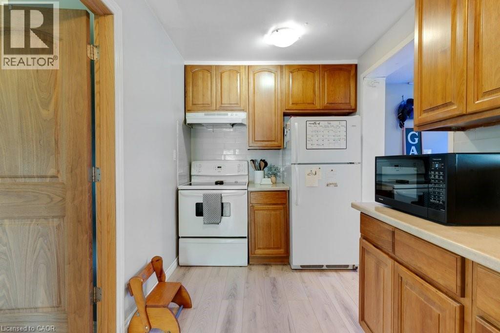 Apartment Kitchen featuring wood cabinetry, light-toned countertops, white tile backsplash, and light wood-finish flooring - 3786 Old Beverly Road, North Dumfries, ON