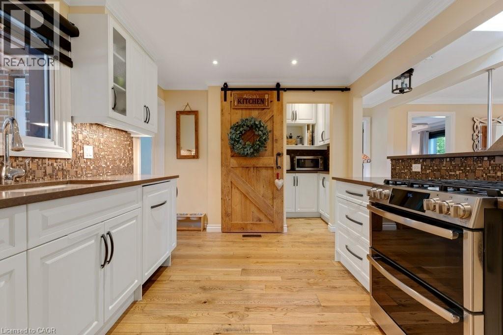 Kitchen featuring wood-finish flooring, white cabinetry with dark hardware, a mosaic tile backsplash, and a stainless steel range - 3786 Old Beverly Road, North Dumfries, ON