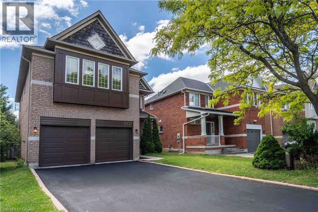 Brick facade residence featuring a two-car garage, asphalt driveway, second-story bay window, and a gabled roofline with shake siding - 2425 Nichols Drive, Oakville, ON - Outdoor