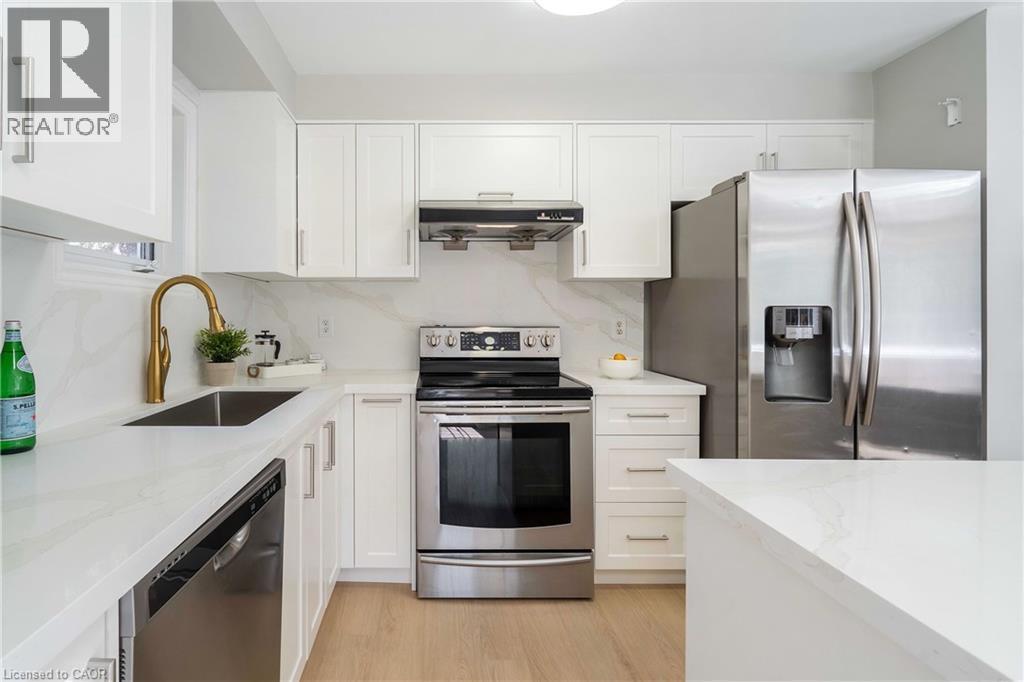 Modern kitchen featuring white cabinetry, stainless steel appliances, light wood-finish flooring, and white countertops with a matching backsplash - 2425 Nichols Drive, Oakville, ON - Indoor Photo Showing Kitchen With Stainless Steel Kitchen With Upgraded Kitchen