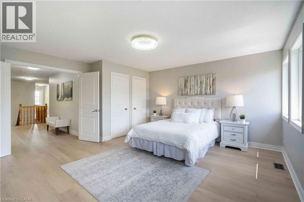Spacious sleeping area featuring light wood-finish flooring, multiple windows, double entry doors, a built-in ceiling light fixture, and an open doorway to a hallway with wood railings - 2425 Nichols Drive, Oakville, ON - Indoor Photo Showing Bedroom