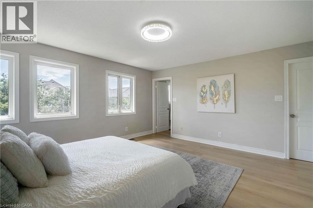 Spacious interior room featuring light wood-finish flooring, multiple windows with white trim, and a contemporary ceiling light fixture - 2425 Nichols Drive, Oakville, ON - Indoor Photo Showing Bedroom