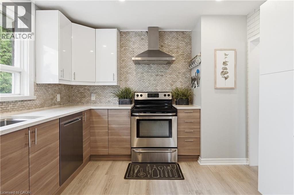 Kitchen featuring wood-finish lower cabinetry, white upper cabinetry, stainless steel appliances, a light-toned mosaic tile backsplash, and light-toned wood-finish flooring - 189 Foxbar Road, Burlington, ON
