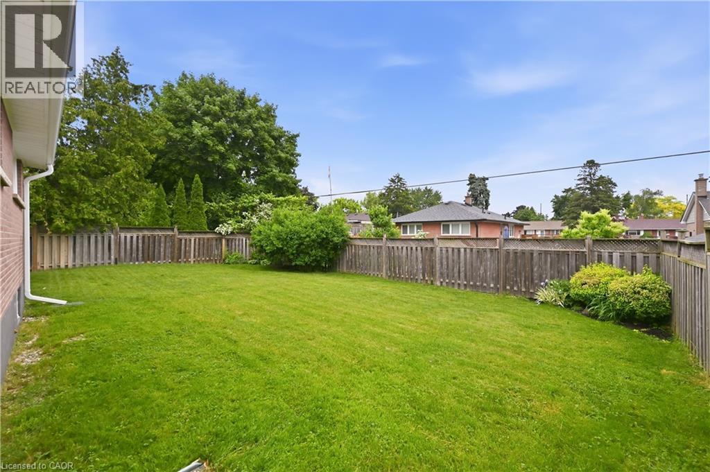 Expansive backyard featuring a manicured lawn, a full-perimeter wood fence, established shrubs, and mature trees - 189 Foxbar Road, Burlington, ON