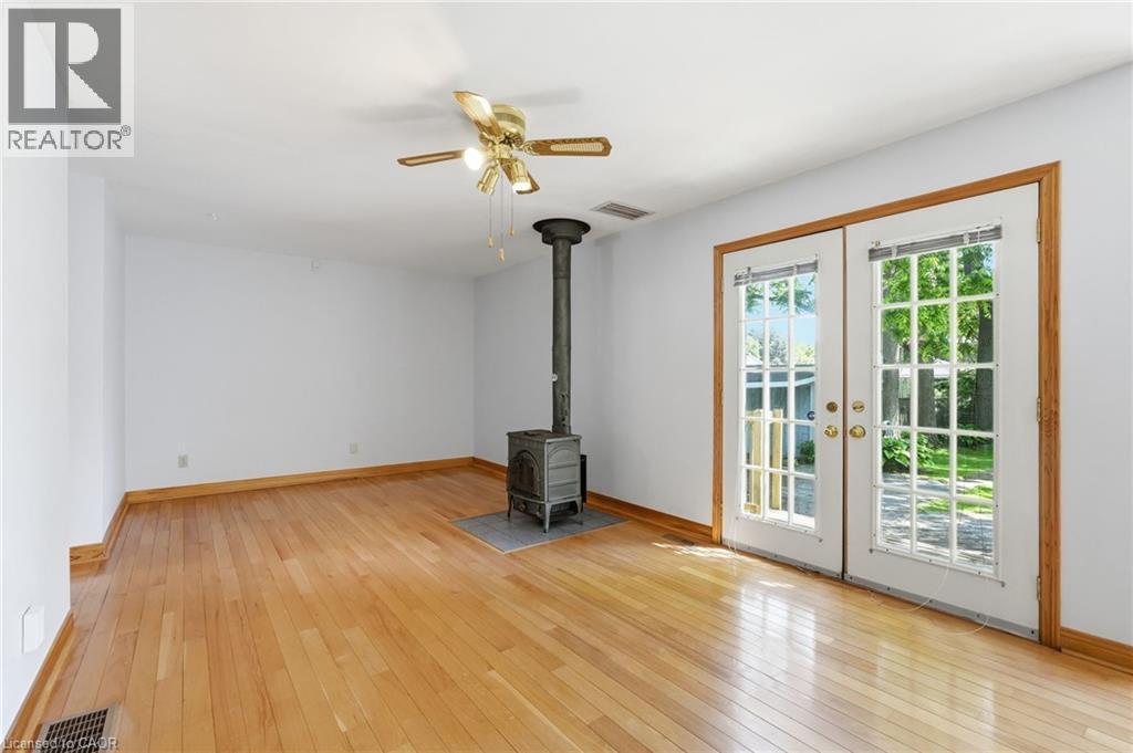 Open room with wood-finish flooring, a freestanding wood-burning stove on a stone-look hearth, and ceiling fan with integrated lighting - 3 Ancaster Street E, Dundas, ON - Indoor Photo Showing Other Room