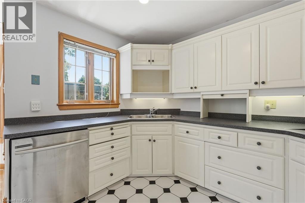 Bright kitchen featuring white cabinetry, dark speckled countertops, and a stainless steel dishwasher - 3 Ancaster Street E, Dundas, ON - Indoor Photo Showing Kitchen With Double Sink