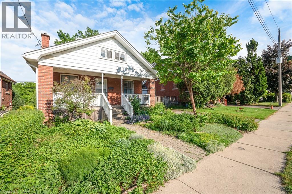 Brick and siding exterior featuring a covered front porch with white railings, a brick chimney, and a paver stone walkway - 295 Keswick Court, Hamilton, ON