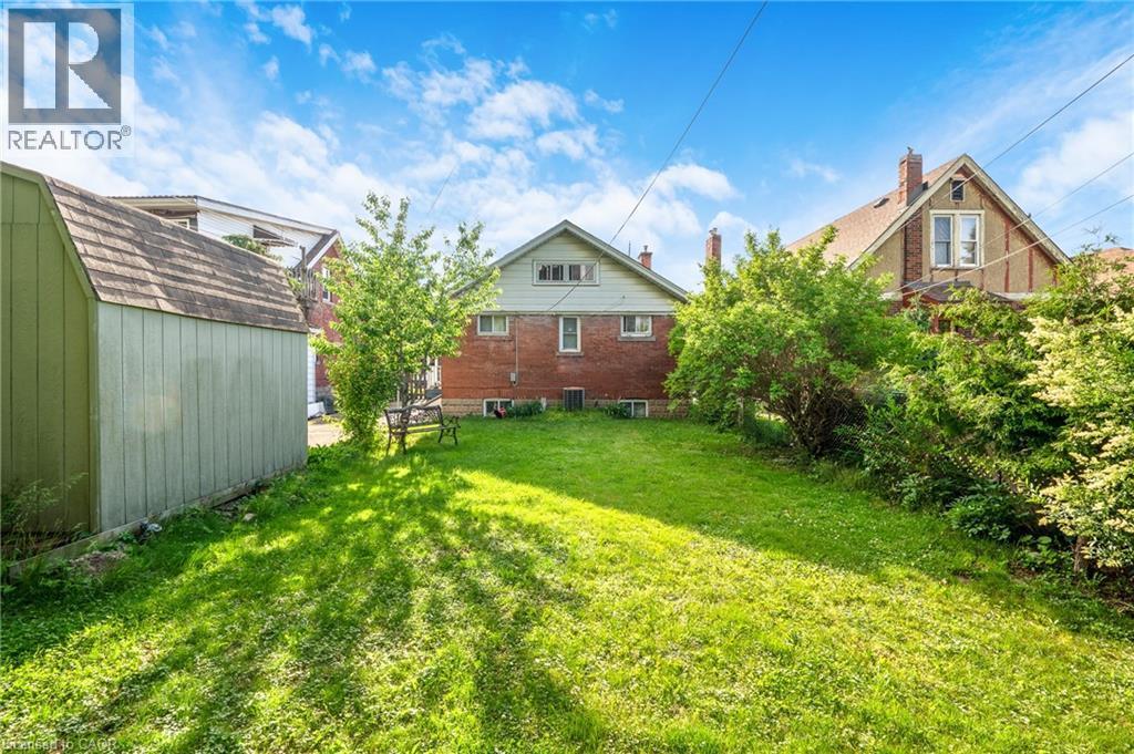Spacious grassy yard with mature trees, a detached storage shed, and a brick exterior home with gabled roofline - 295 Keswick Court, Hamilton, ON