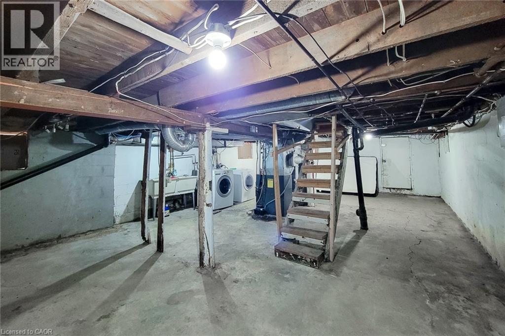 Unfinished basement featuring a utility sink, laundry hookups, exposed wooden ceiling joists, and a partial staircase - 463 Wellington Street N, Hamilton, ON - Indoor Photo Showing Basement
