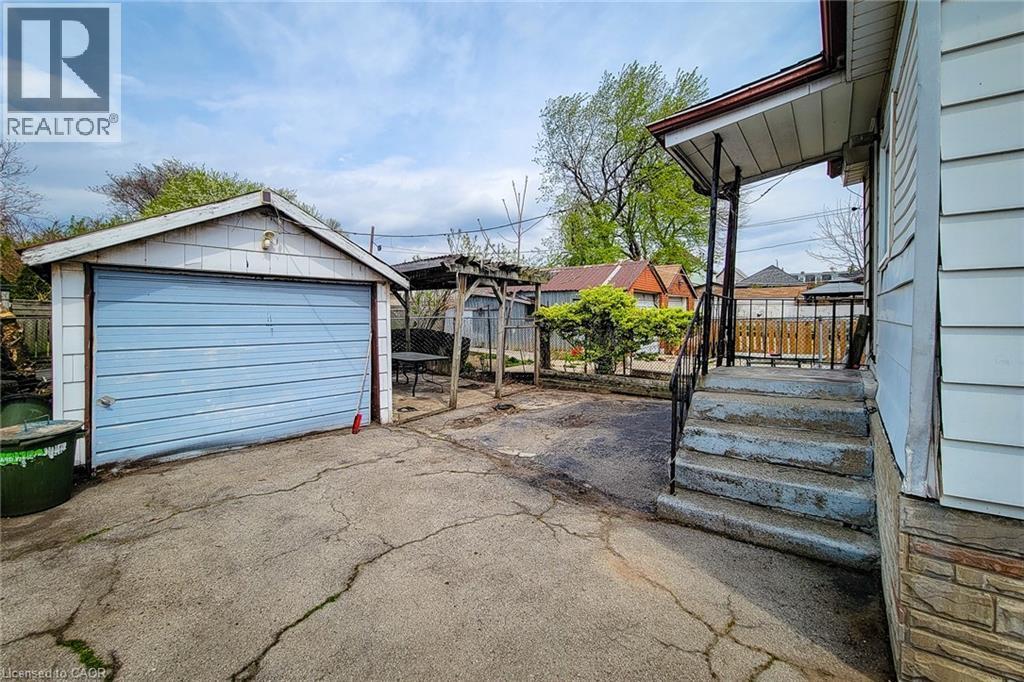Detached garage with light blue garage door, concrete driveway, stone veneer foundation, covered porch with black metal railing, and a wooden pergola structure - 463 Wellington Street N, Hamilton, ON - Outdoor