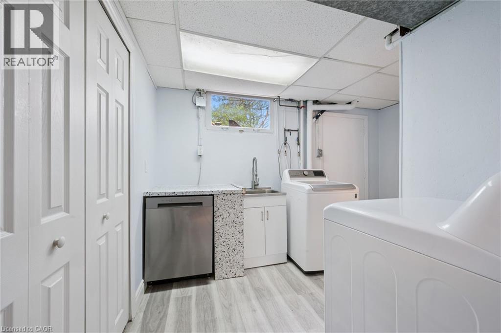 Dedicated laundry area featuring wood-finish flooring, a utility sink with a chrome faucet, white cabinetry, and a window providing natural light - 176 Woodville Place, Waterloo, ON - Indoor Photo Showing Laundry Room