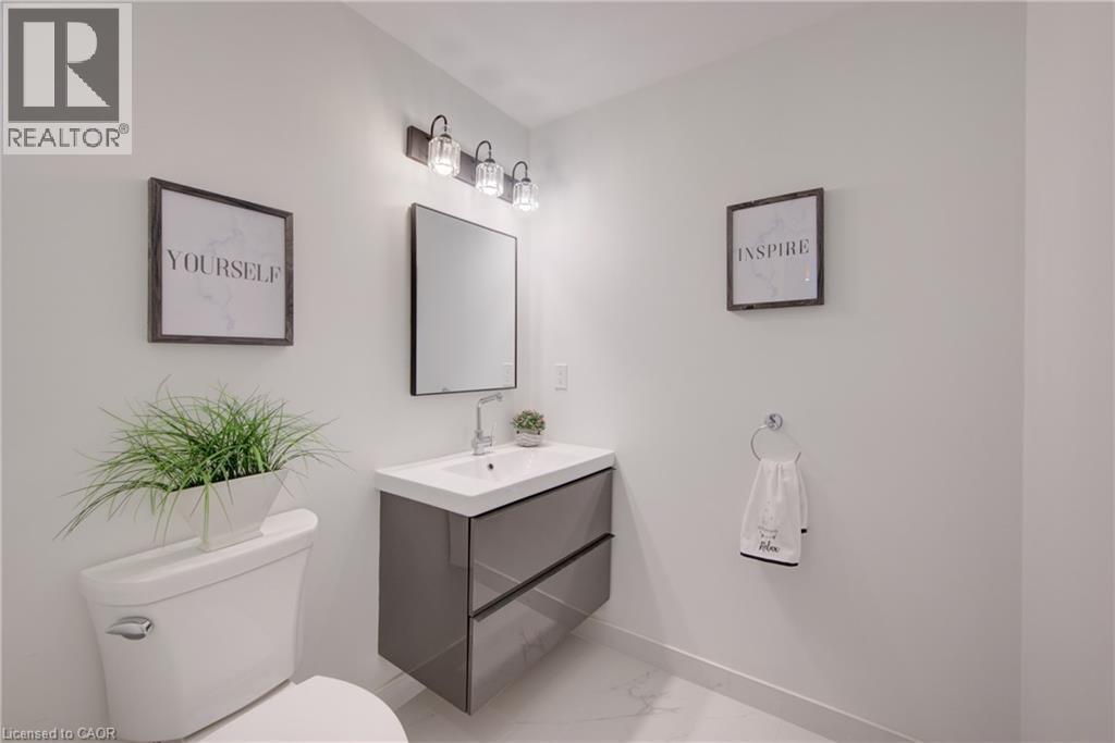 Bathroom featuring a floating vanity with integrated sink, a rectangular mirror, a three-light fixture with clear glass shades, a ceramic toilet, and large format floor tiles - 191 King Street S Unit# 607, Waterloo, ON