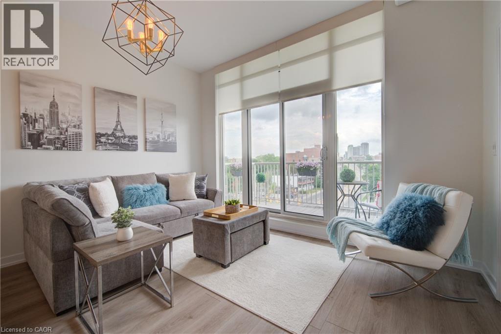 Living space featuring wood-finish flooring, a contemporary geometric chandelier, and full-height windows with roller shades - 191 King Street S Unit# 607, Waterloo, ON