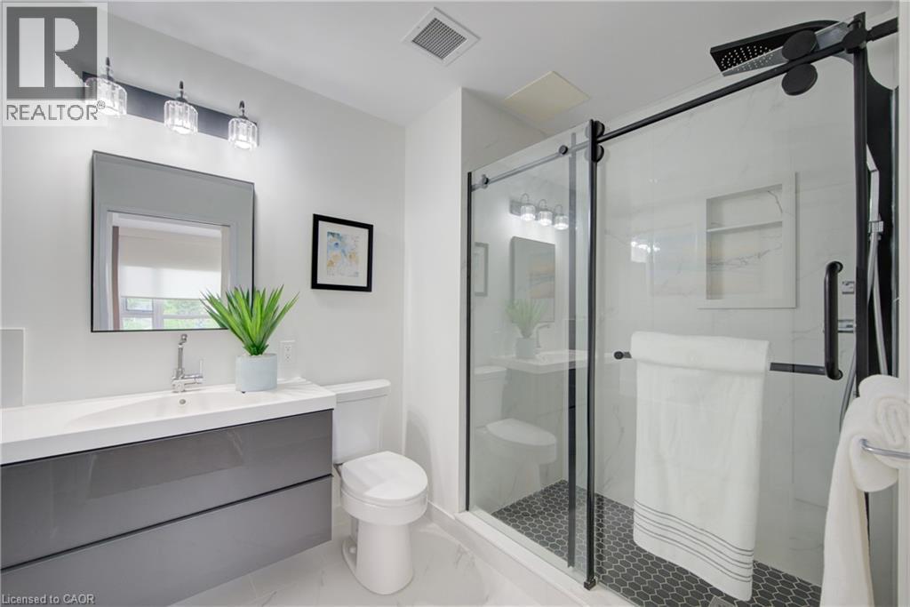 Modern bathroom featuring a floating vanity with a white countertop and integrated sink, a frameless rectangular mirror, and a three-light fixture with clear glass shades - 191 King Street S Unit# 607, Waterloo, ON