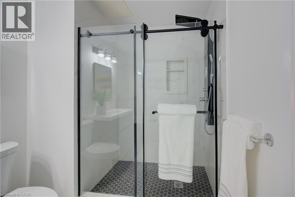 Spacious shower enclosure with black-framed glass sliding doors, black hexagonal tile flooring, and a built-in shower niche - 191 King Street S Unit# 607, Waterloo, ON