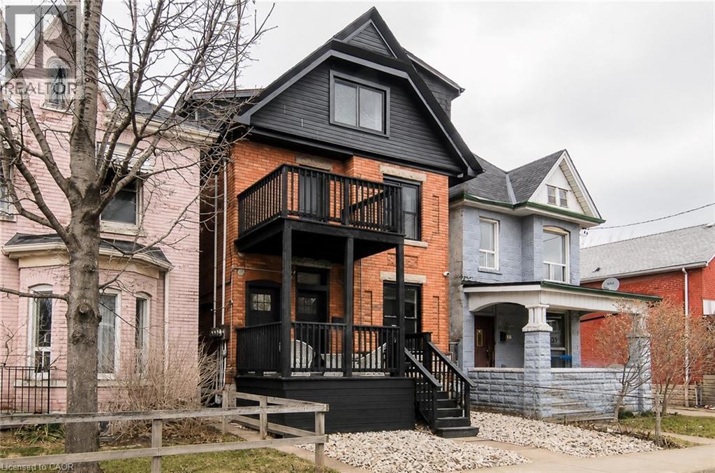 Brick facade home featuring a dormer roofline, two-story balconies with dark railings, and exterior stairs - 249 Emerald Street N, Hamilton, ON