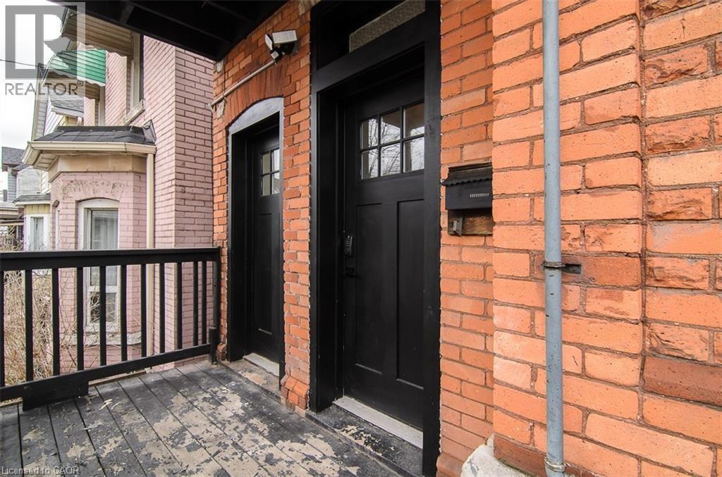 Brick exterior featuring two black entry doors with divided lites, a black wooden railing, and a black mailbox - 249 Emerald Street N, Hamilton, ON
