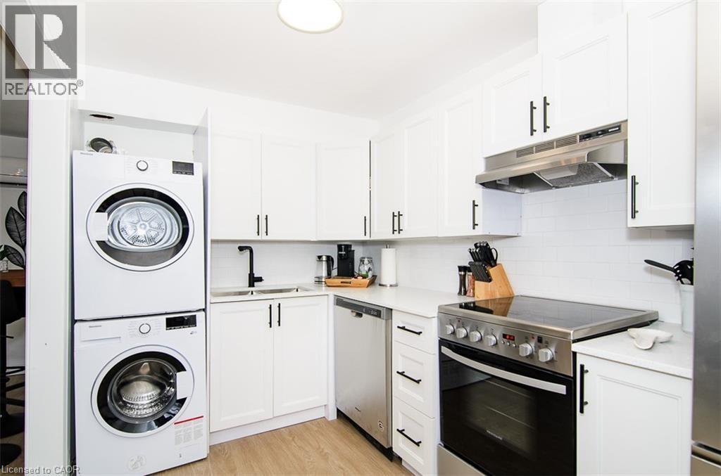 Modern kitchen featuring white shaker cabinetry with matte black hardware, white subway tile backsplash, a stainless steel range with overhead ventilation, and an integrated stackable washer and dryer - 249 Emerald Street N, Hamilton, ON
