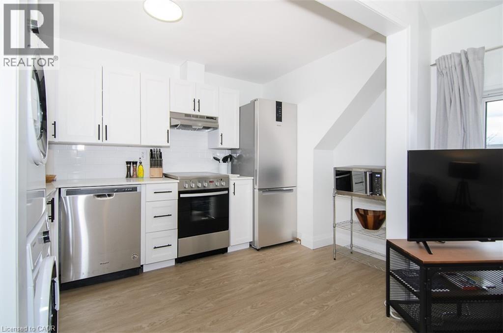 Kitchen area featuring white shaker-style cabinetry with matte black hardware, stainless steel appliances, light-colored wood-finish flooring, white subway tile backsplash, and a white countertop - 249 Emerald Street N, Hamilton, ON
