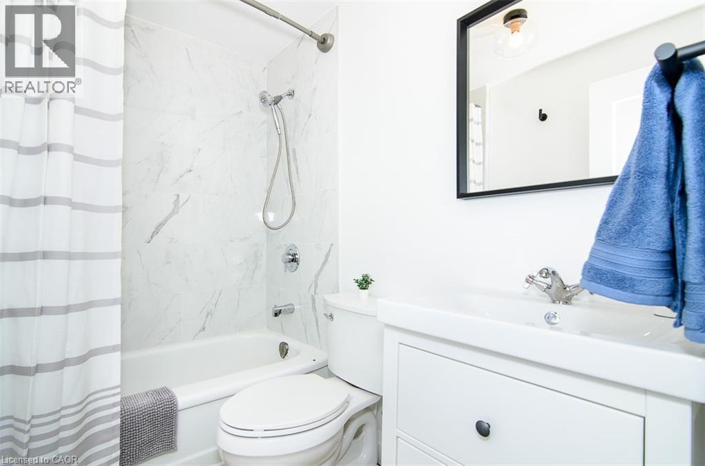 Bathroom featuring a white bathtub with a tile surround, a built-in toilet, and a vanity with a rectangular basin - 249 Emerald Street N, Hamilton, ON