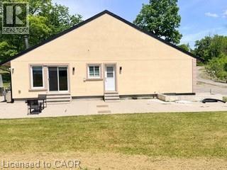 Rear exterior featuring a stucco finish, black roofline, sliding glass doors with steps, a white entry door with steps, and an expansive concrete patio - 10631 Fifth Line, Milton, ON