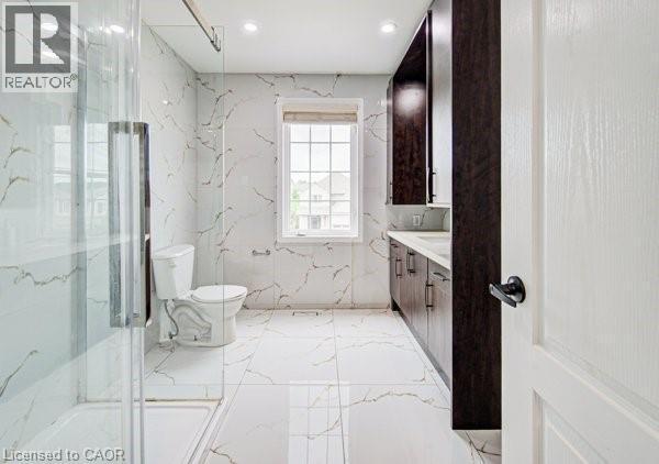 Bathroom featuring a glass-enclosed shower, white tile flooring, white tile walls with gold veining, dark wood-finish cabinetry, and a window providing natural light - 55 Isaiah Drive, Kitchener, ON
