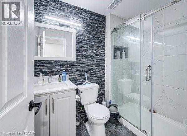 Bathroom featuring a textured accent wall, white vanity with integrated sink, framed mirror, and a glass-enclosed shower with a built-in niche - 55 Isaiah Drive, Kitchener, ON