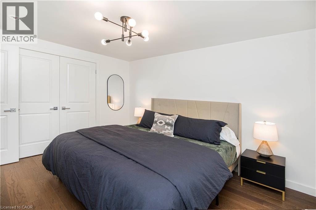 Bedroom featuring wood-finish flooring, a modern sputnik-style ceiling light, and white paneled doors - 39 Forestgate Drive, Hamilton, ON