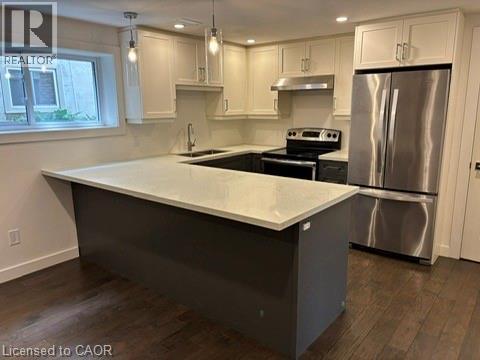 Modern kitchen featuring a U-shaped island with a light-colored countertop, dark gray cabinetry, stainless steel appliances, and wood-finish flooring - 39 Forestgate Drive, Hamilton, ON