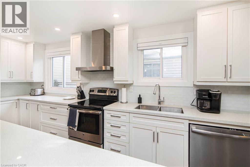 Contemporary kitchen featuring white shaker cabinetry, stainless steel appliances, a double basin sink, light-toned countertops, and subway tile backsplash - 39 Forestgate Drive, Hamilton, ON