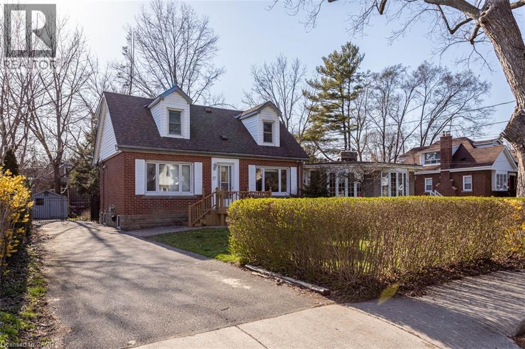 Traditional brick facade residence featuring a front entry with wood steps, two dormer windows, a paved driveway, and a detached storage shed - 17 Thorndale Street N, Hamilton, ON
