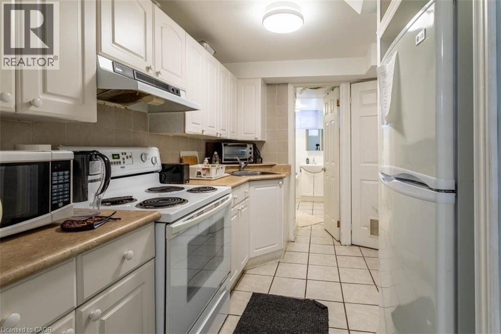 Efficient kitchen space featuring white cabinetry with traditional knobs, a built-in range hood, neutral-toned countertops, and square tile flooring - 17 Thorndale Street N, Hamilton, ON
