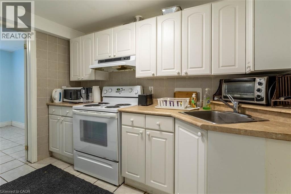 Kitchen featuring white cabinetry, light-toned countertops, a full-size range, and a double-basin sink - 17 Thorndale Street N, Hamilton, ON