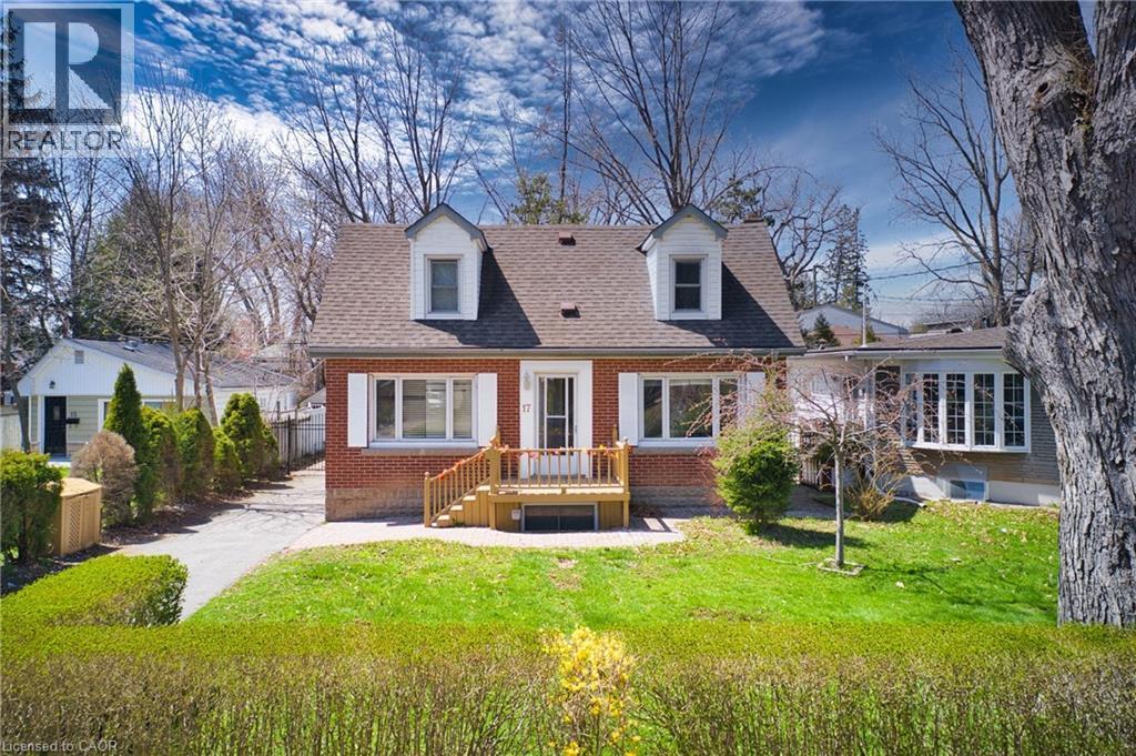 Brick residence featuring a gabled roofline with two dormer windows, a front wooden deck, and a manicured front lawn - 17 Thorndale Street N, Hamilton, ON