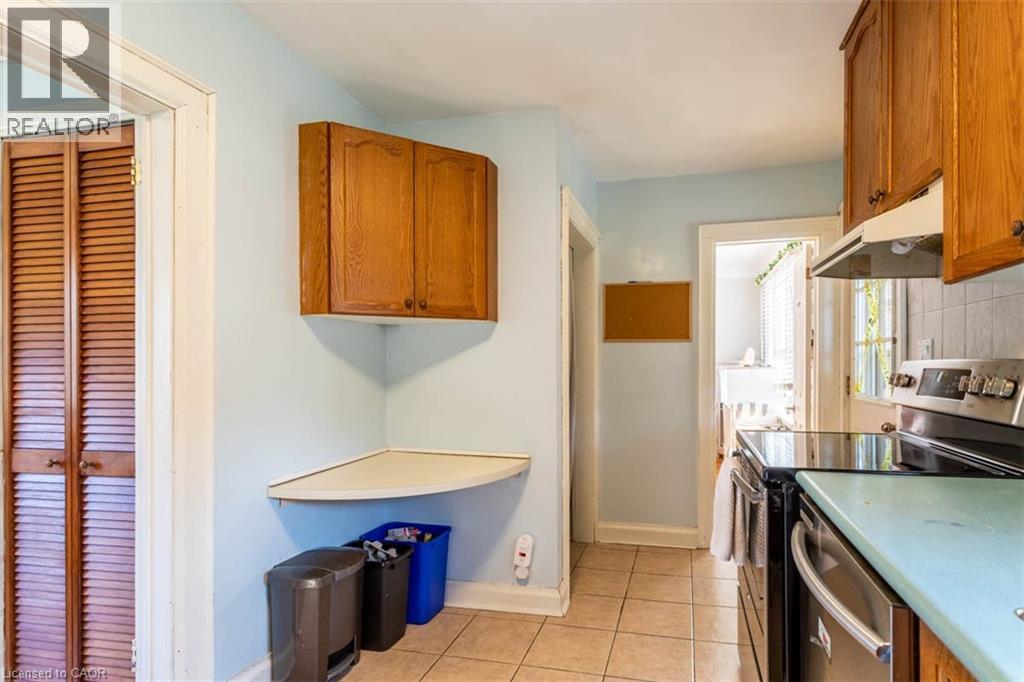 Kitchen featuring a stainless steel range with a black ceramic cooktop, a coordinating exhaust hood, wood cabinetry, and a tile backsplash - 17 Thorndale Street N, Hamilton, ON