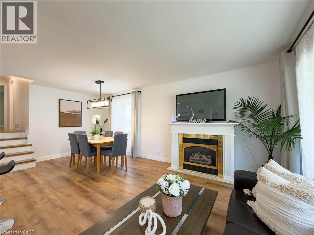 Open-concept living space with wood-finish flooring, a white mantel fireplace with a brass-accented insert, and a dining area featuring a contemporary chandelier - 1324 Bodley Road, Mississauga, ON