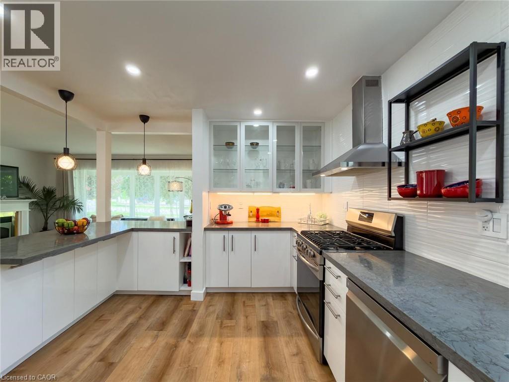 Contemporary kitchen featuring wood-finish flooring, white cabinetry, integrated stainless steel appliances, a range hood, and a textured white tile backsplash - 1324 Bodley Road, Mississauga, ON