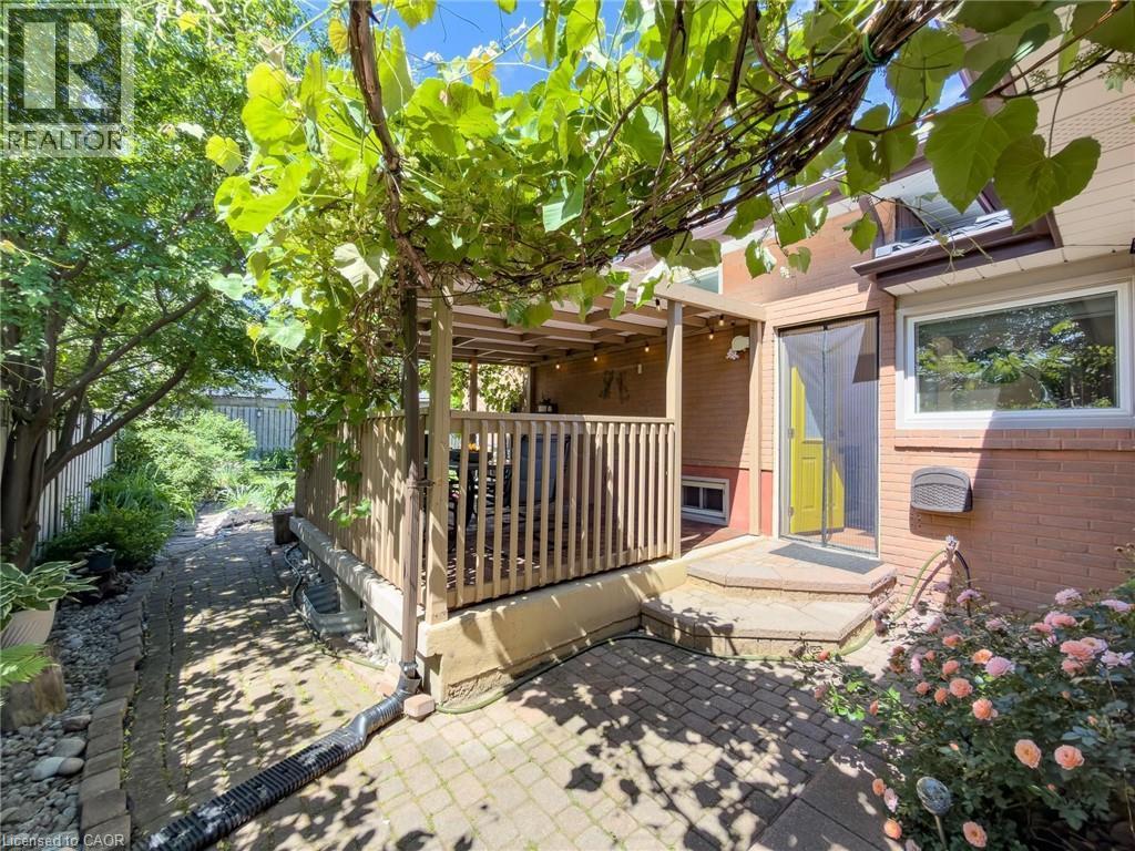 Outdoor patio area featuring a covered deck with wooden railings, a yellow-painted exterior door, and a brick paver patio - 1324 Bodley Road, Mississauga, ON
