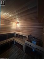 Dedicated sauna room featuring extensive wood paneling, built-in multi-level seating, a wall-mounted light fixture, and a sauna heater with stones -