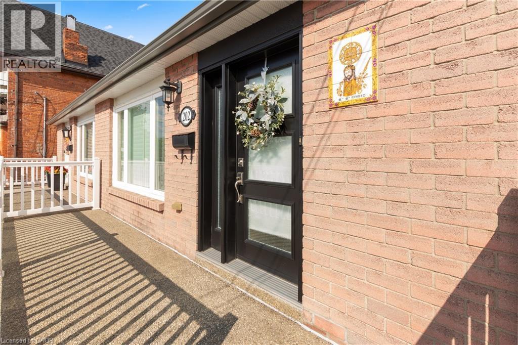 Brick exterior featuring an entry door with frosted glass panels, an exterior wall sconce, and a white framed window. - 202 Ray Street N, Hamilton, ON - Outdoor With Exterior
