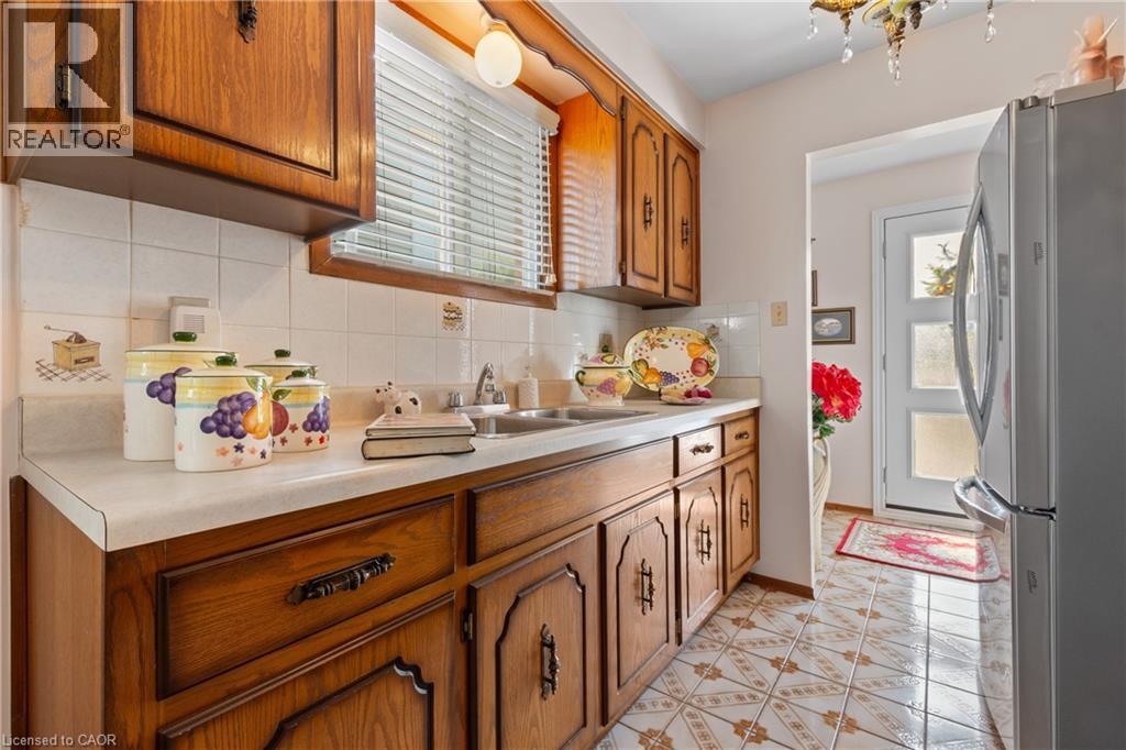 Kitchen featuring wood cabinetry, a white laminate countertop, a stainless steel double basin sink, and white ceramic tile backsplash. - 202 Ray Street N, Hamilton, ON - Indoor Photo Showing Kitchen With Double Sink